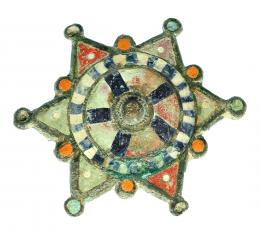 ROMA. Bajo Imperio. Bronce y pasta vítrea. Fíbula con forma de estrella hexagonal con umbo central. Con decoración de pasta vítrea polícroma. Altura: 5,4 cm. Procedente de colección privada española años 1970-80.