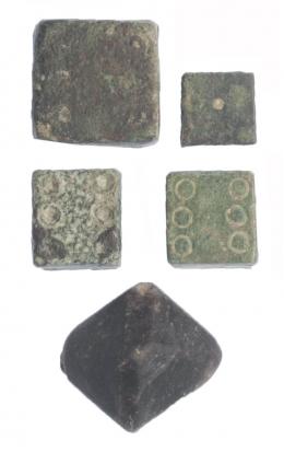 516  -  TARDOANTIGÜEDAD. VI-VIII d.C. Bronce y jaspe negro. Lote de 5 objetos: cuenta de collar romboide y 4 dados.  8 x 8 - 15 x 15 mm.
