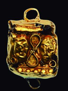 BIZANCIO. Elemento decorativo (VII-IX d.C.). Oro. Forma cúbica con representación de dos cabezas masculinas en cada cara. Dos arandelas en la parte superior y una inferior. Dimensiones 21 x 13 mm.