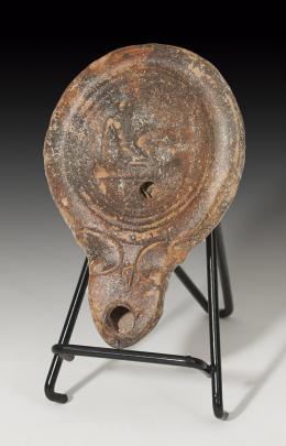 ROMA. Imperio Romano. Lucerna (I-II d.C.). Cerámica. Arcilla anaranjada, piquera biselada, un orificio de llenado y disco central decorado con escena erótica. Longitud 11,9 cm.