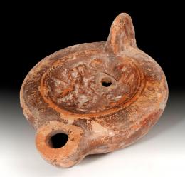 ARQUEOLOGÍA. ROMA. Imperio Romano. Lucerna (II d.C.). Cerámica. Pasta anaranjada, piquera circular, dos agujeros de llenado y disco central decorado con escena erótica. Longitud 13 cm.