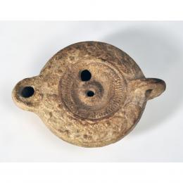 ROMA. Imperio Romano. Lucerna con decoración vegetal y geométrica, con piquera circular y dos agujeros de llenado. Terracota. Longitud 11,5 cm.
