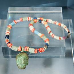 2070   -  ARQUEOLOGÍA. PREHISPÁNICO. Moche. Collar con rostro antrompomorfo, a modo de colgante, tallado por los cuatro lados. Crisocola y espondilo en forma de cuentas. Longitud 27 cm.