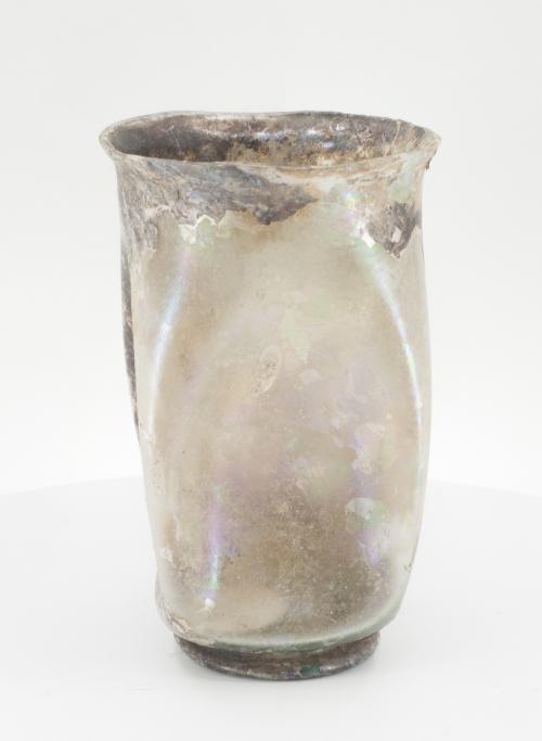 500 - ROMA. Imperio Romano. Mediados II- mediados III d.C. Vidrio. Vaso cilíndrico con rehundimientos. Presenta irisaciones. Altura 11,0 cm.