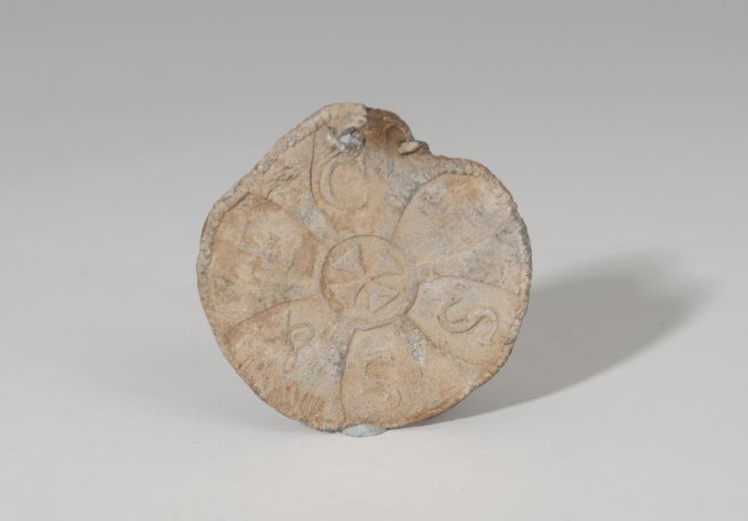 486   -  EDAD MODERNA. Placa circular (XV-XVI d.C.). Plomo. Cruz central e inscripción alrededor. Diámetro 4,1 cm.