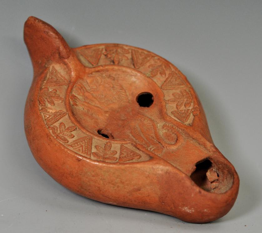 2052   -  ARQUEOLOGÍA. PERIODO PALEOCRISTIANO. Lucerna con piquera circular, un agujero de llenado y disco central, decorado con un león y figuras geometricas. Siglos V-VI d .C. Terracota. Longitud 13 cm.