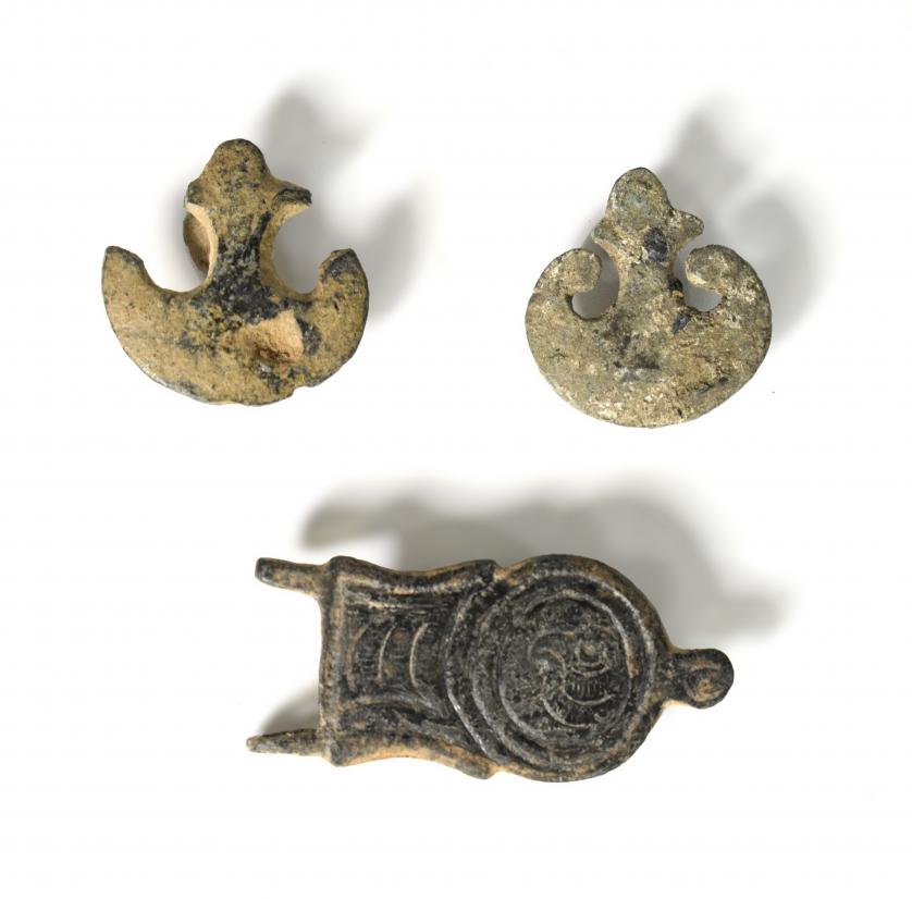 2075   -  ROMA y PERÍODO VISIGODO. Lote de 2 botones dobles y una hebilla (ss. III d.C. y VII-VIII d.C.). Dos con forma de pelta o flor de lis y hebilla liriforme con campo cuadrado con decoración geométrica y circular con decoración de cabeza de águila. Altura botones 2,8 y 2,9 cm. Longitud hebilla 5,1 cm.