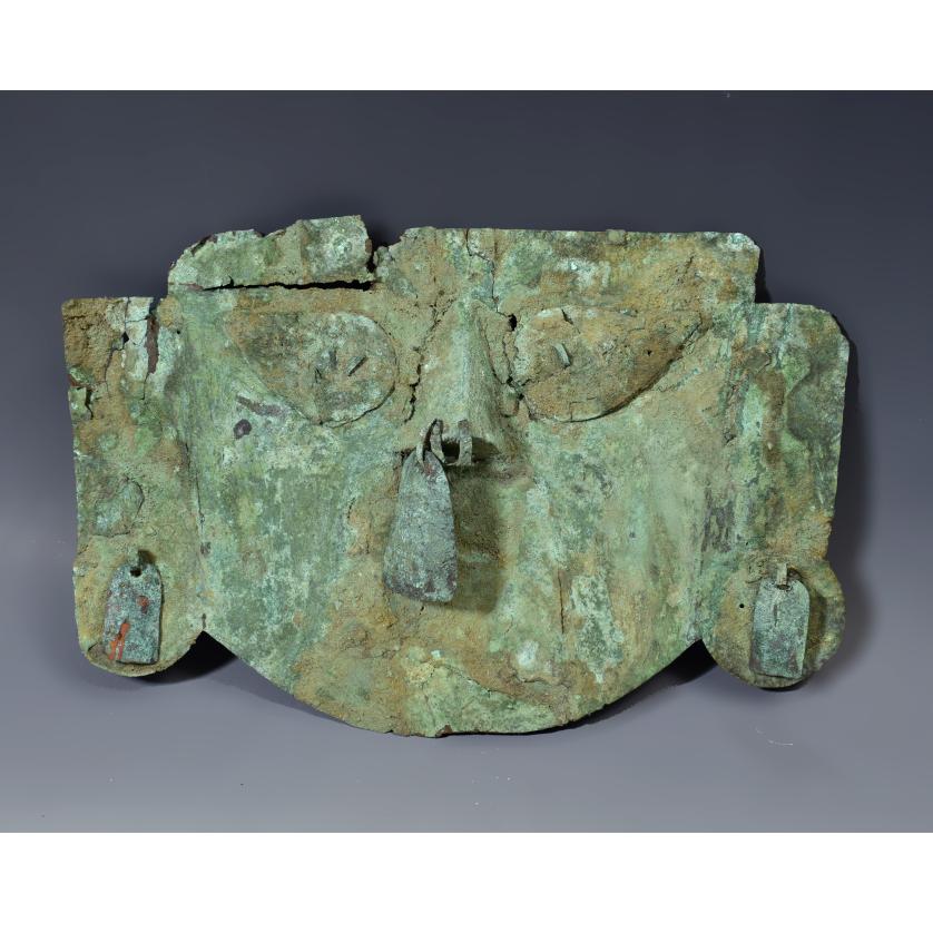 2041   -  ARQUEOLOGÍA. PREHISPÁNICO. Fragmento de pectoral en forma de máscara, representando al dios Neylan. Cultura Sicán (700-1375 d.C.). Cobre. Algunas pérdidas y grietas. Longitud 25 cm x 16,5 cm.